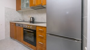 A modern kitchen with wooden cabinets, a stainless steel refrigerator, a built-in oven, and a kettle. - Apartment Vukorepa (Razanj)