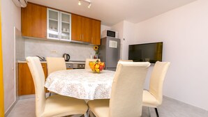 A compact kitchen with wooden cabinets, a refrigerator, a microwave, and a dining table with four chairs. - Apartment Vukorepa (Razanj)