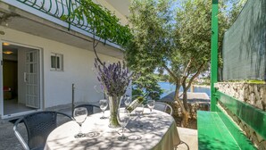 An outdoor dining area with a table set for two, surrounded by chairs, and a vase with flowers. - Apartment Vukorepa (Razanj)