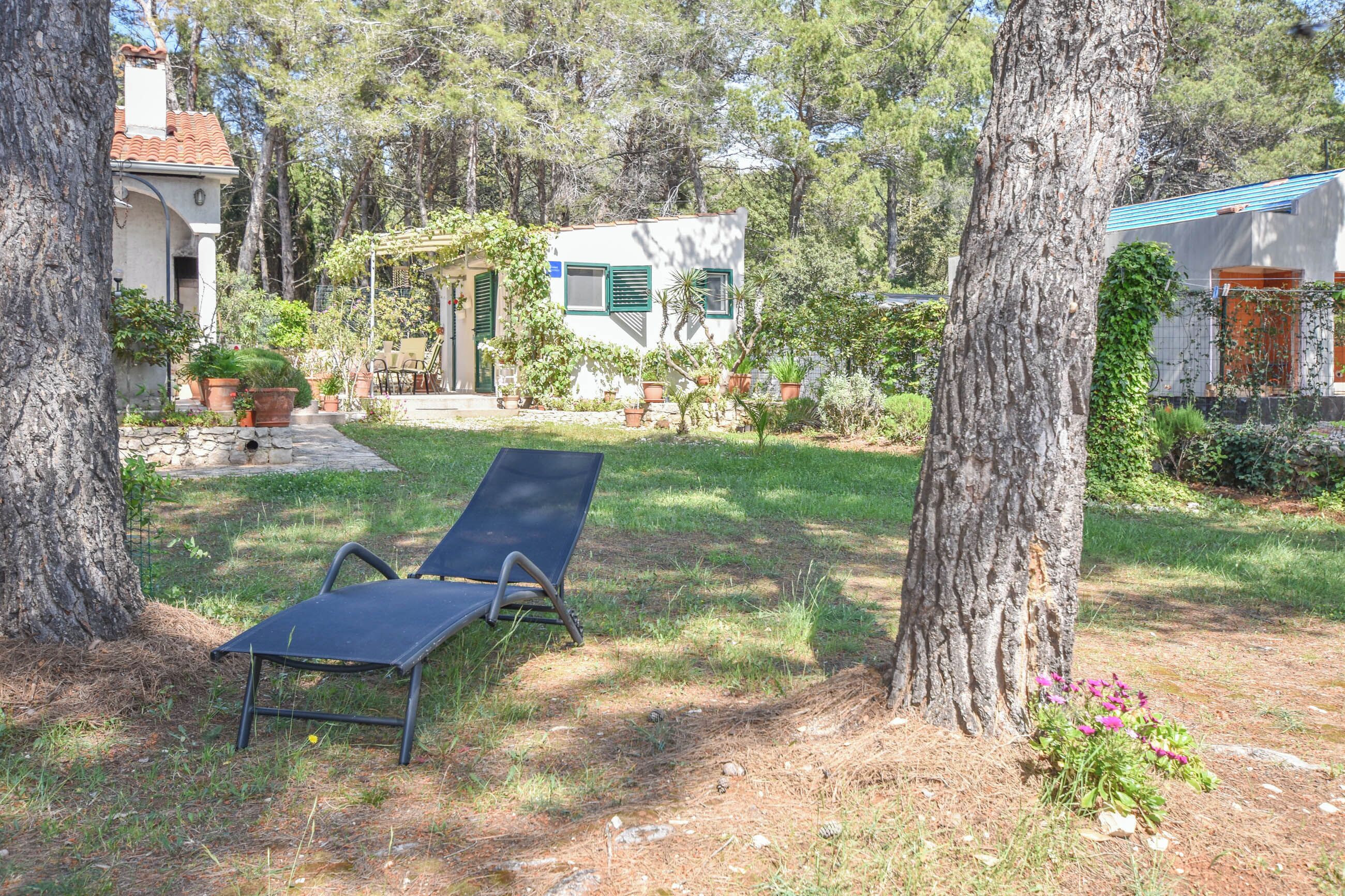 A garden with a lounge chair, a small house with a green door, and potted plants.