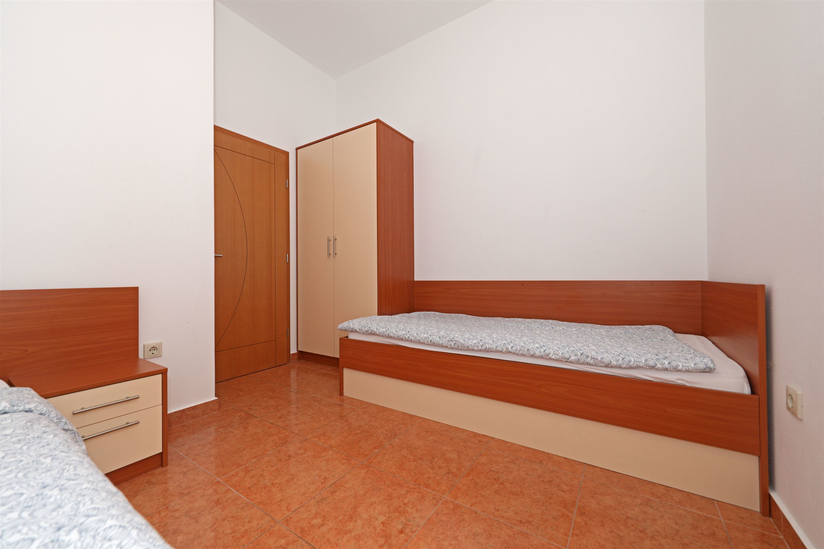 A bedroom with a wooden bed, a nightstand, a wardrobe, and a door.