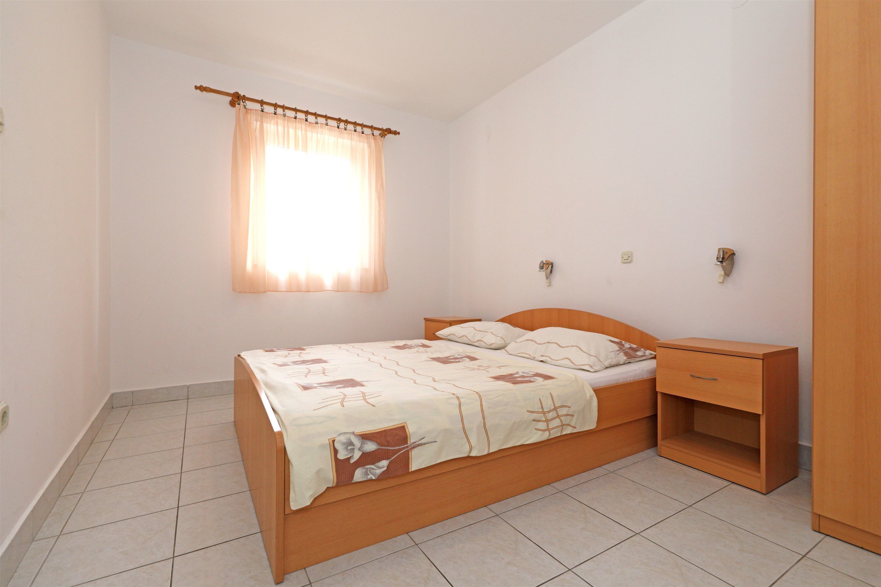 Een slaapkamer met een enkel bed, een nachtkastje, een houten kledingkast en een raam met gordijn.