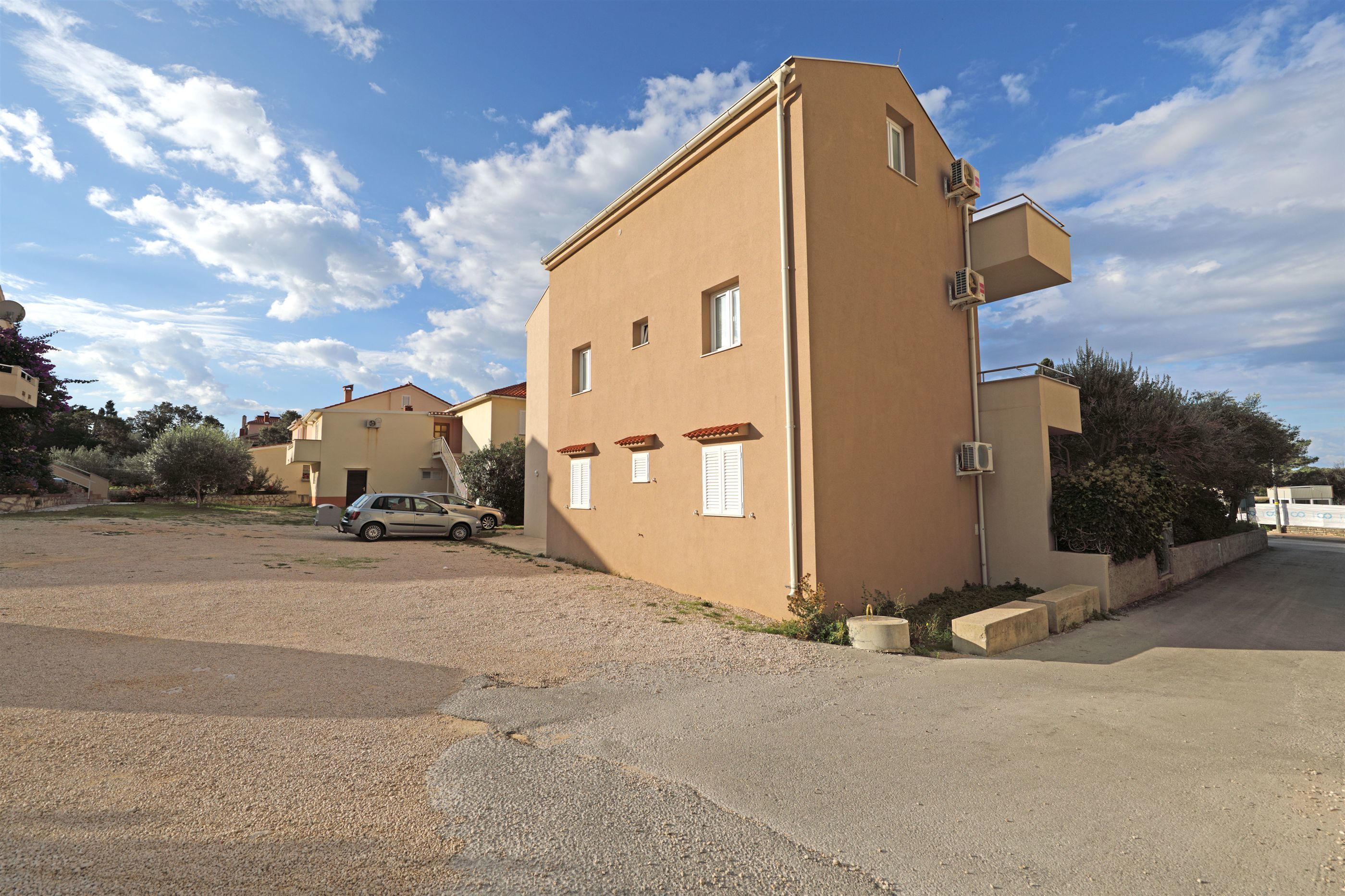 A residential building with a beige exterior, multiple windows, and a car parked in the driveway.