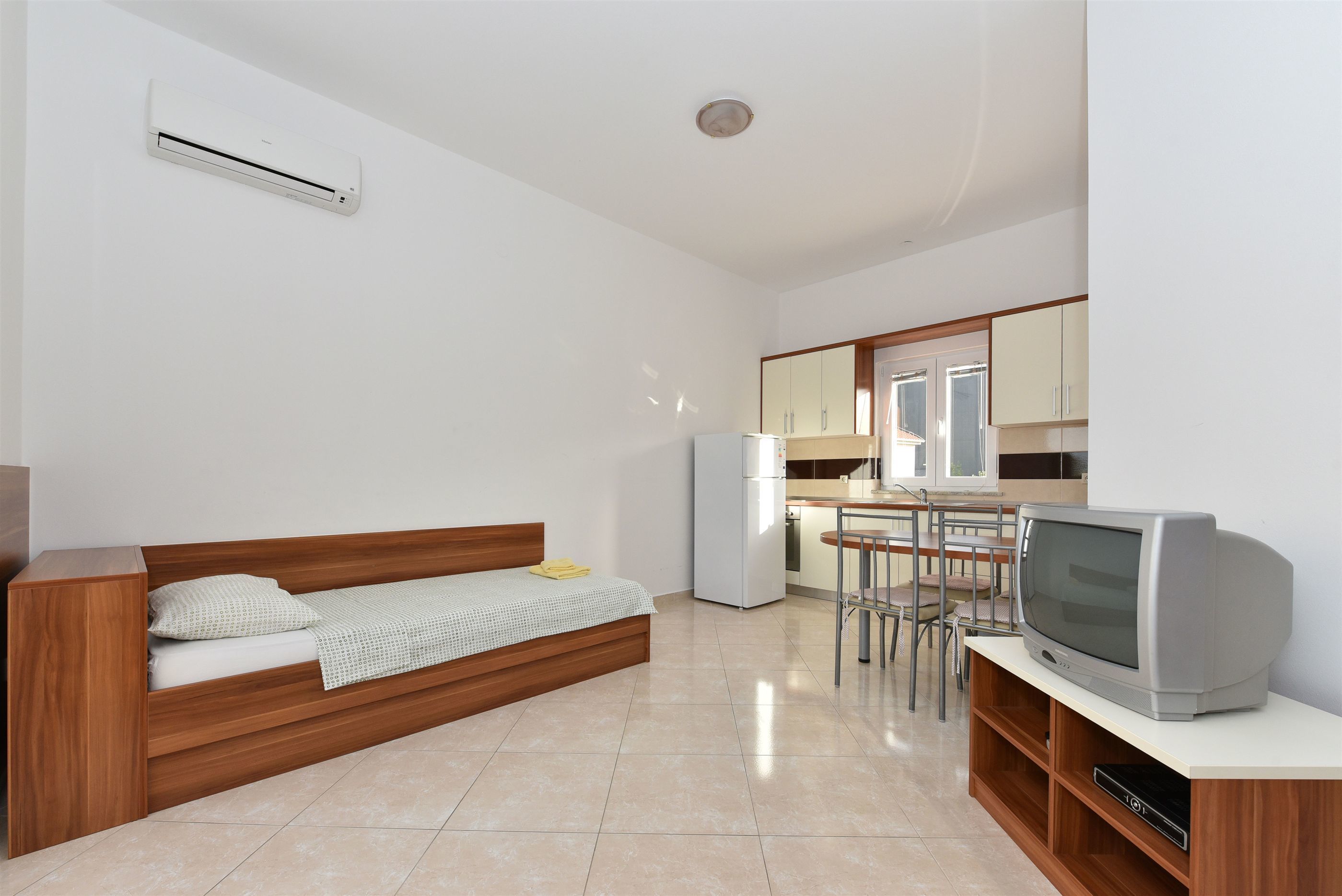 Um espaço de estar moderno e compacto, com cama, cozinha compacta e televisão.