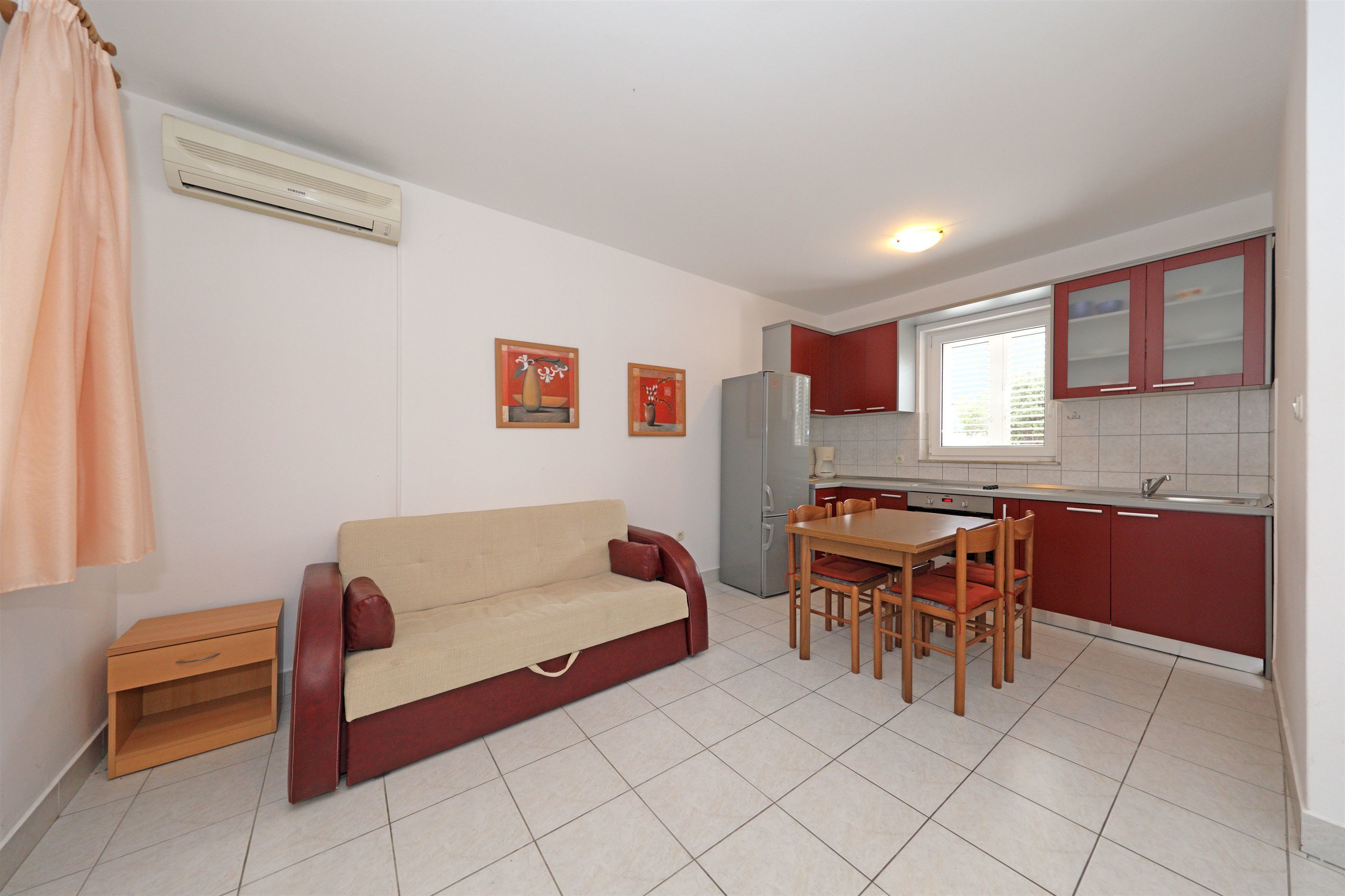A compact living space with a kitchenette, a sofa, a dining table with chairs, and a small cabinet.