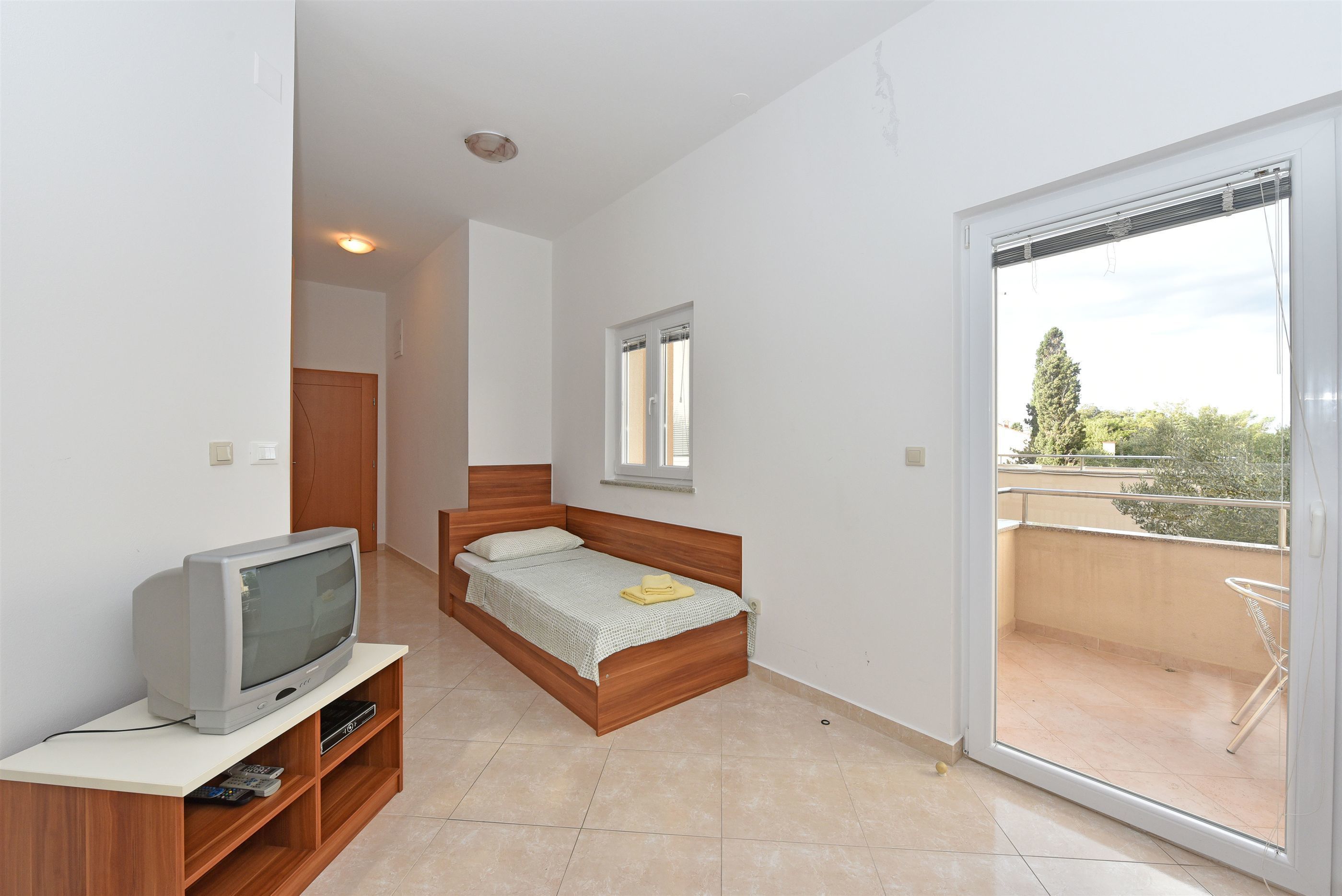 Une chambre à coucher avec un lit, un téléviseur posé sur un meuble, une fenêtre et un balcon.