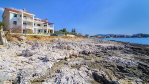 A coastal property with a multi-story building, rocky shoreline, and a clear view of the sea. - Apartment Lavanda (Rogoznica)
