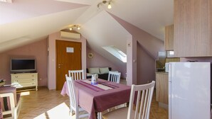 A dining area with a table set for four, a television, and a kitchen area with a refrigerator and cabinets. - Apartment Lavanda (Rogoznica)