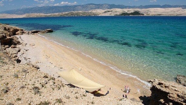 A beach with clear turquoise water, rocky terrain, and a tent set up on the shore. - Apartment Marija (Kolan)