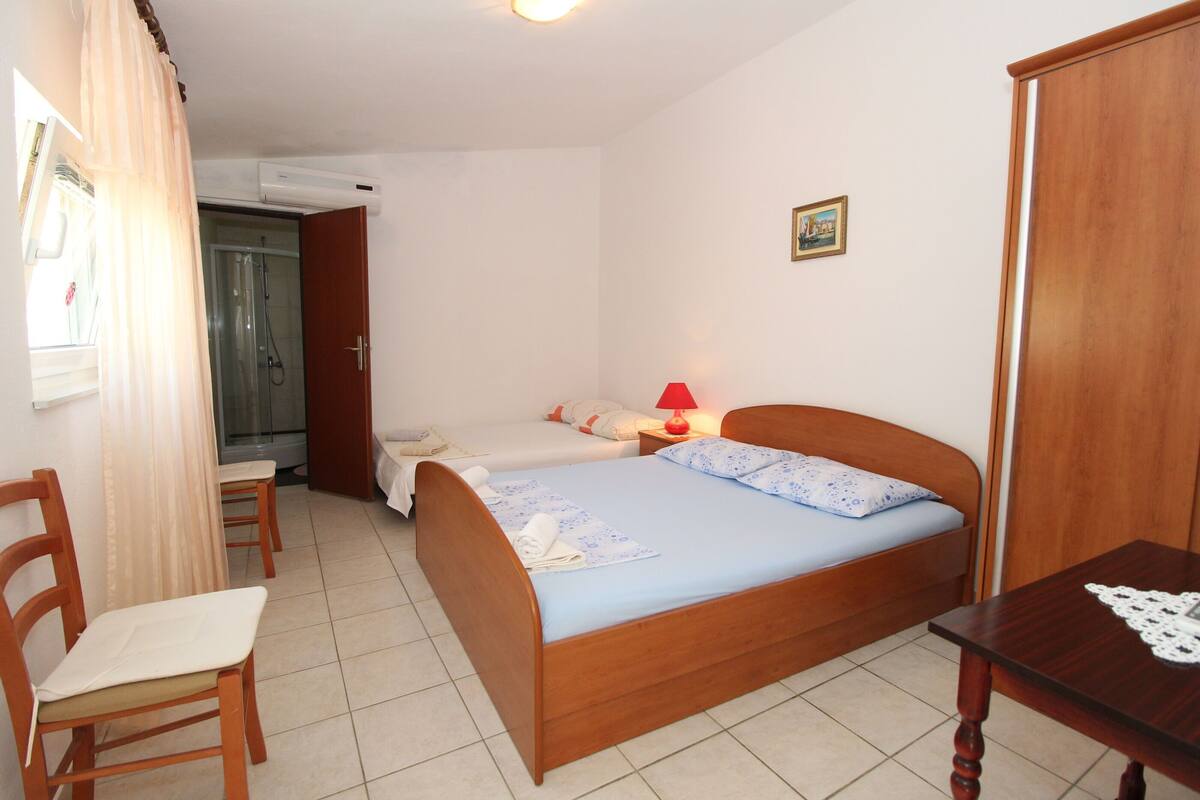 Une chambre à coucher avec un lit en bois, deux tables de chevet, une chaise, une petite table et une fenêtre avec des rideaux.
