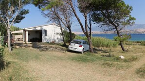 A white building with a garage, parked car, and a view of the sea and mountains. - Apartment Marija (Kolan)