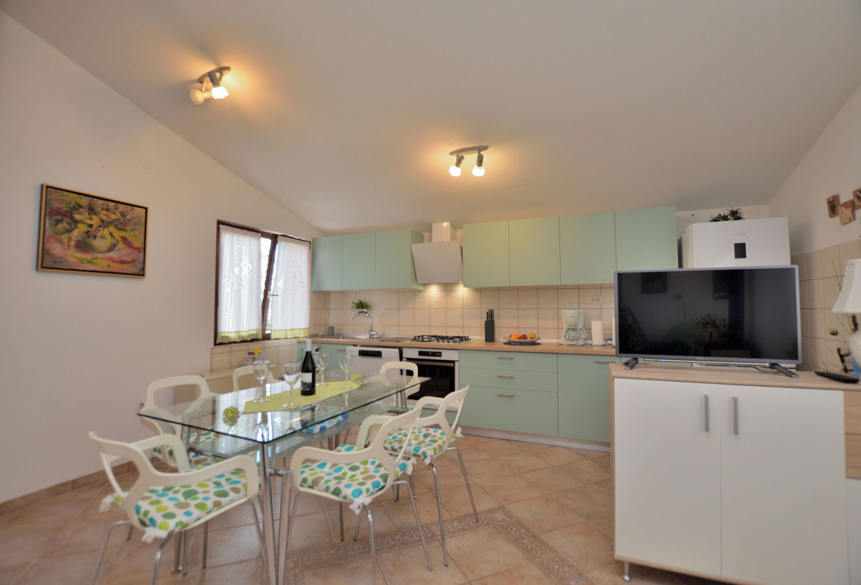 A modern kitchen with a glass dining table, white chairs, and a built-in TV.