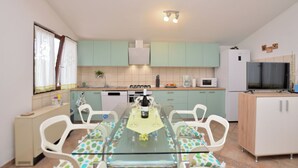 A compact kitchen with a dining table set for four, a microwave, a stove, and a refrigerator. - House Marlu (Rakalj)