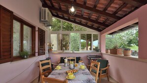 A dining area with a table set for four, wooden chairs, a window with shutters, and potted plants on the windowsill. - House Marlu (Rakalj)