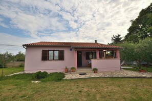 A pink single-story house with a tiled roof, a front porch, and potted plants. - House Marlu (Marcana)