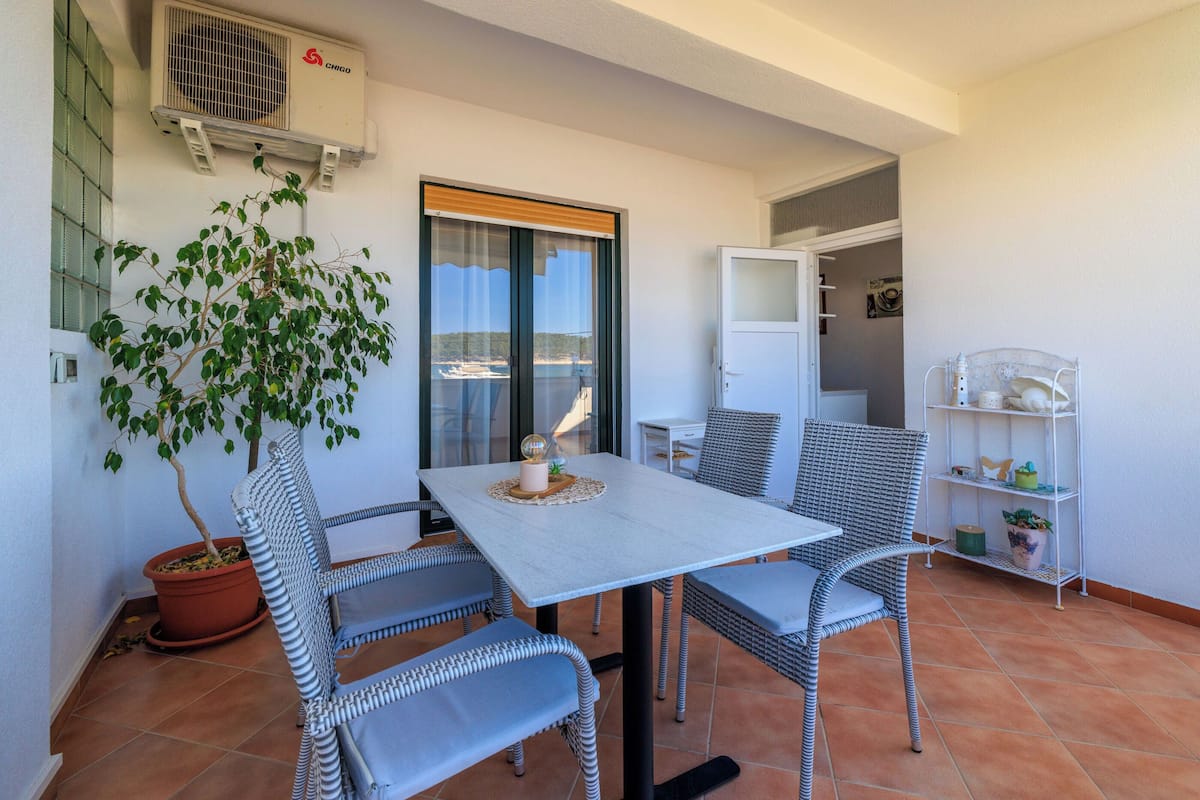 A balcony with a table and chairs, a potted plant, and a white shelf with decorative items.
