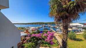 A marina with boats, a palm tree, and a building with a balcony overlooking the water. - Apartments Near the sea Barbat (Barbat)