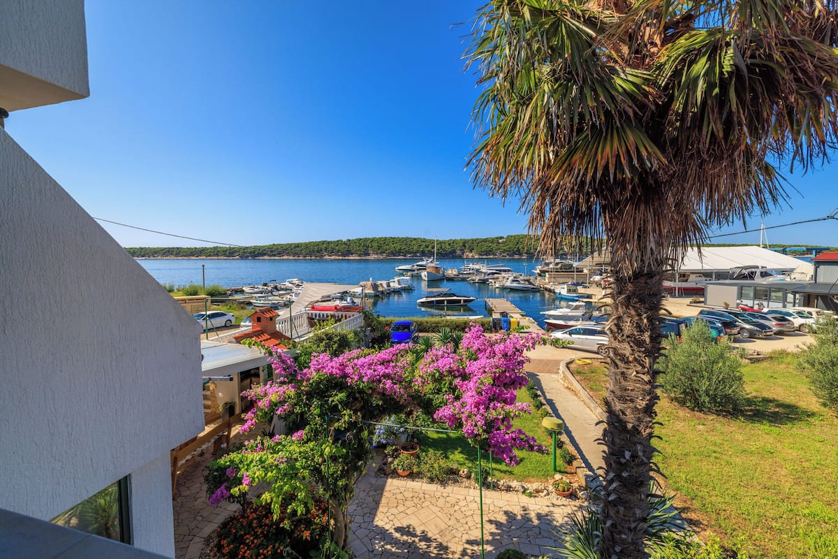 A marina with boats, a palm tree, and a building with a balcony overlooking the water.