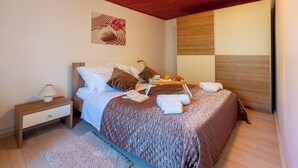 Un lit bien fait, recouvert d’une couverture marron, une table de chevet avec une lampe, et un plateau contenant des serviettes et un livre.