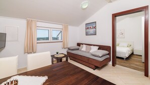 A modern living room with a wooden dining table, a sofa, and a bed in the adjacent room. - House Ljerka (Barbat)