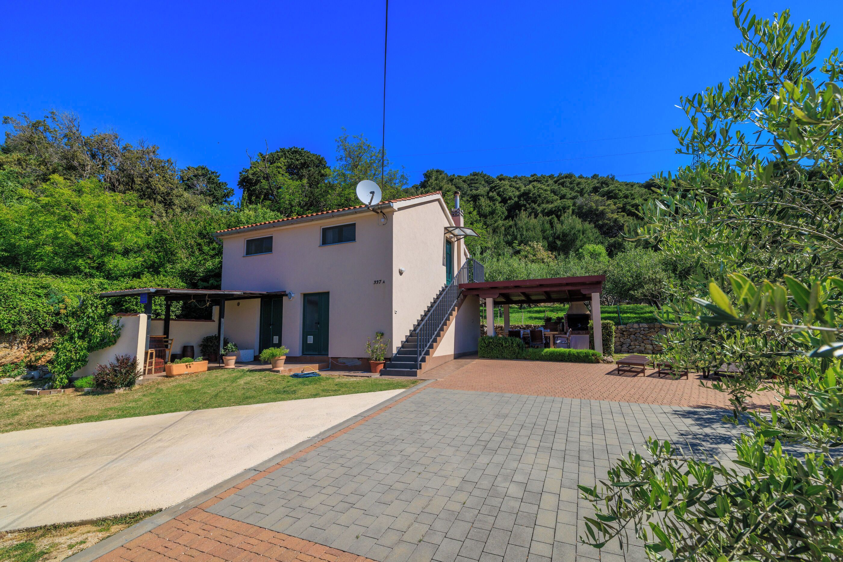 Ein zweistöckiges Haus mit überdachter Terrasse, Satellitenschüssel und gepflasterter Auffahrt.