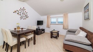 A modern living room with a dining table, sofa, TV, and decorative wall art. - House Ljerka (Barbat)