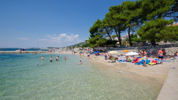 A beach with clear water, people swimming and sunbathing, and trees along the shore. - House Ljerka (Barbat)