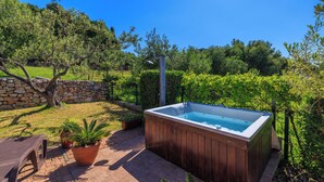 A hot tub in a backyard with a stone wall, potted plants, and a patio chair. - House Ljerka (Barbat)