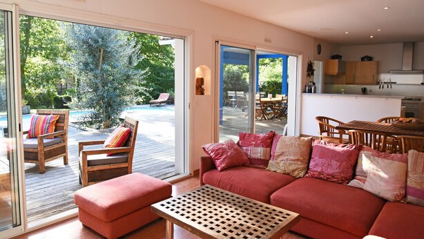A spacious living room with a red sofa, a wooden coffee table, and a sliding glass door leading to a pool area. - exceptional, quiet, golf on 27 holes character villa, heated pool (Biscarrosse)