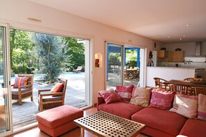 Un salon spacieux avec un canapé rouge, une table basse en bois et une porte-fenêtre coulissante donnant sur une zone abritant une piscine.
