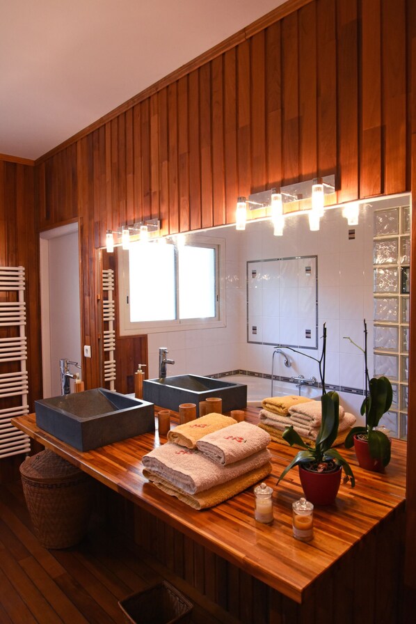 Une salle de bain aux murs lambrissés, dotée d’un grand miroir, de deux vasques et d’un meuble-lavabo en bois.
