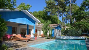 A poolside area with a wooden deck, lounge chairs, and a clear blue pool. - exceptional, quiet, golf on 27 holes character villa, heated pool (Biscarrosse)
