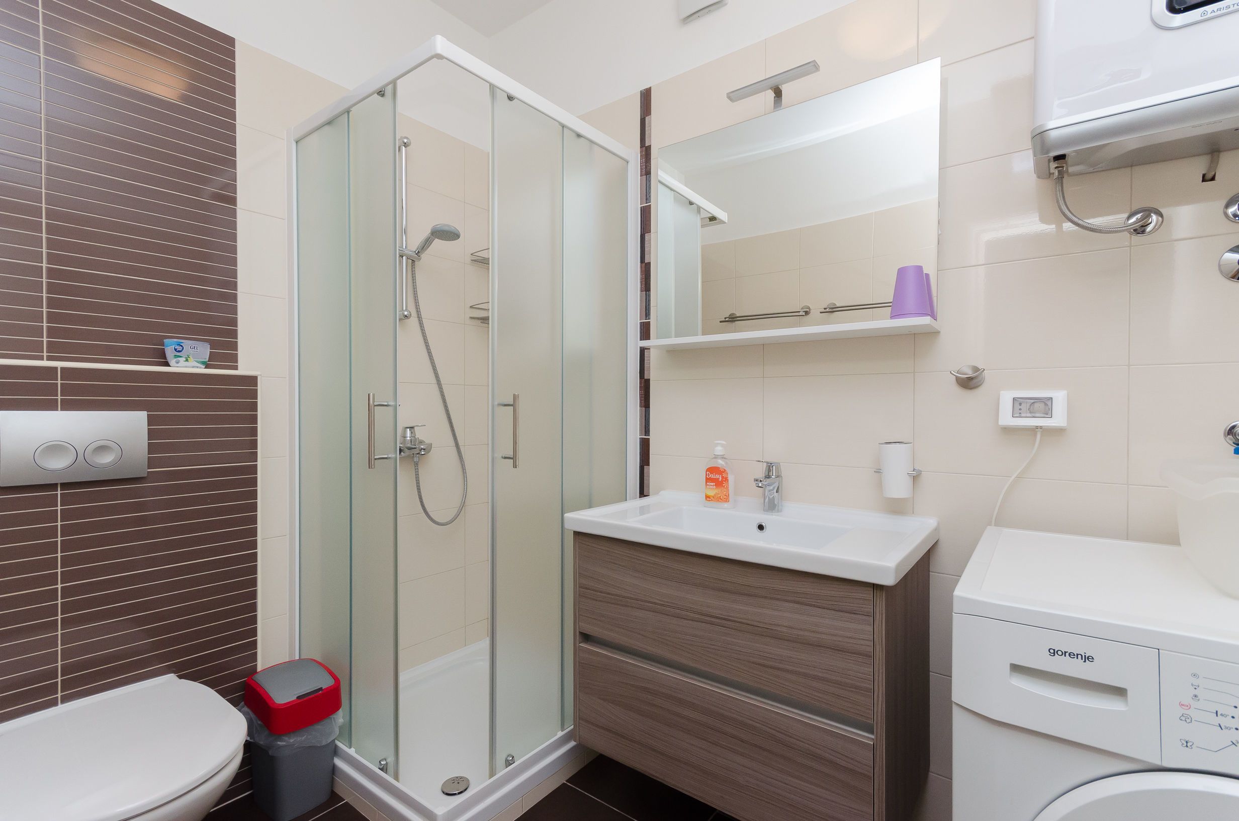 A modern bathroom with a glass shower enclosure, a white sink with a wooden vanity, and a toilet.