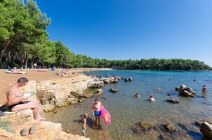 A beach with clear water, rocky shoreline, and people swimming and relaxing.