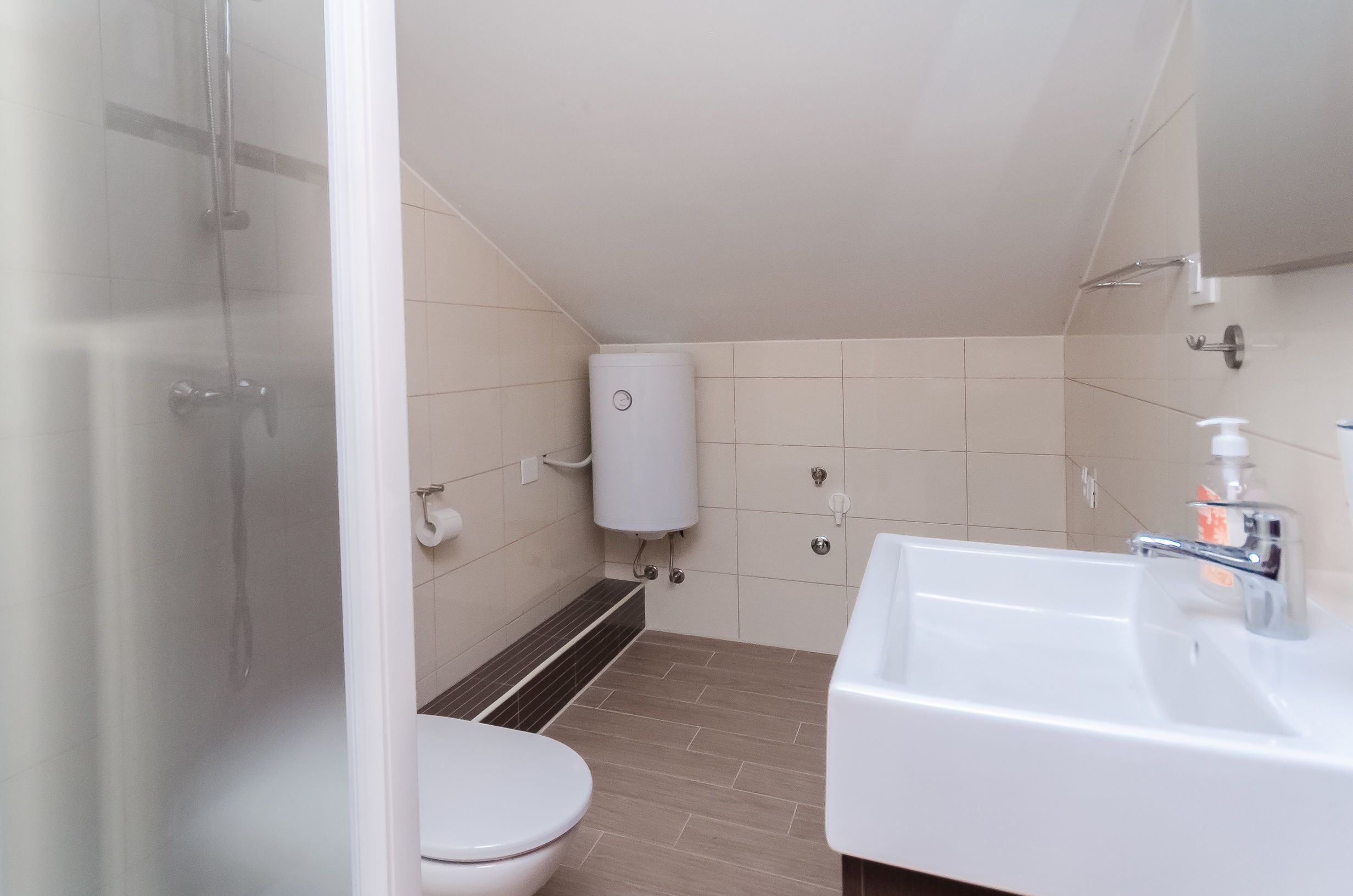 Un baño pequeño con inodoro, lavamanos, ducha y dispensador de papel higiénico.