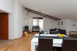 A modern living room with a dining area, featuring a wooden floor, white walls, and a sloped ceiling.