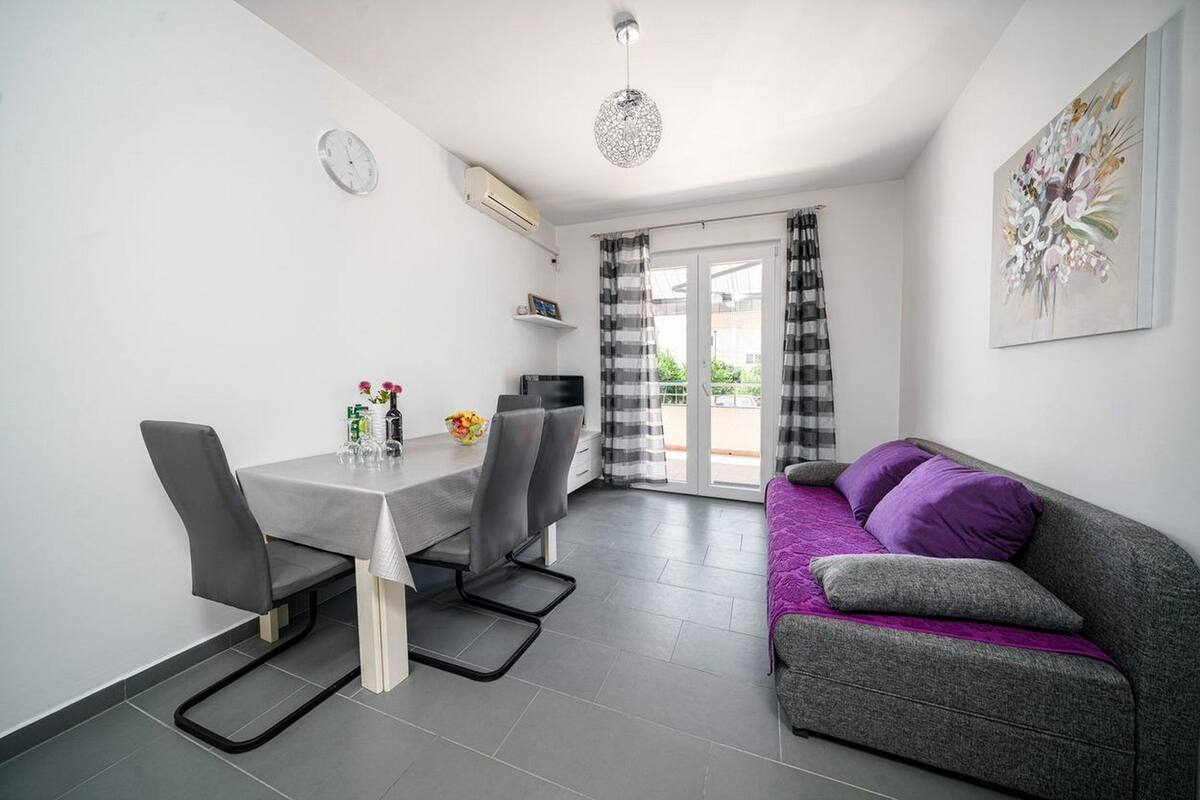 A modern living room with a grey sofa, a dining table with chairs, and a large window with curtains.