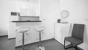 Una cucina moderna con mobili bianchi, un forno a microonde e un angolo bar con due sgabelli.