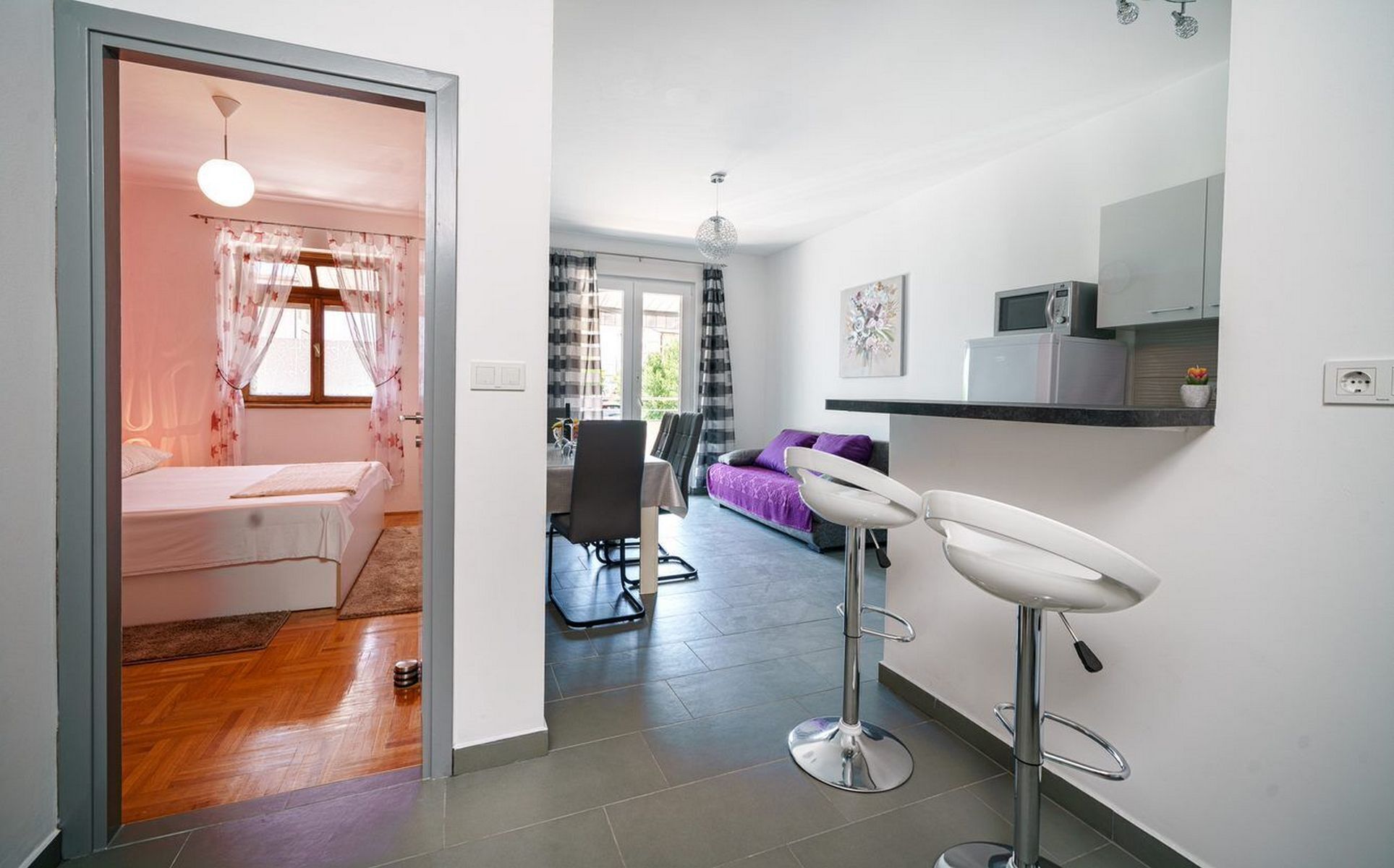 Una sala de estar moderna con un sofá, una zona de comedor con un taburete de bar y una cocina con microondas.