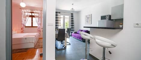A modern living room with a sofa, a dining area with a bar stool, and a kitchen area with a microwave.