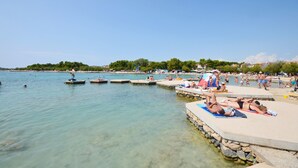 Una spiaggia con acque cristalline, persone che prendono il sole e un pontile con barche.