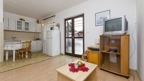 A compact kitchen with a dining area, a television on a wooden stand, and a door leading outside. - Apartments Tonin (Ivan Dolac)