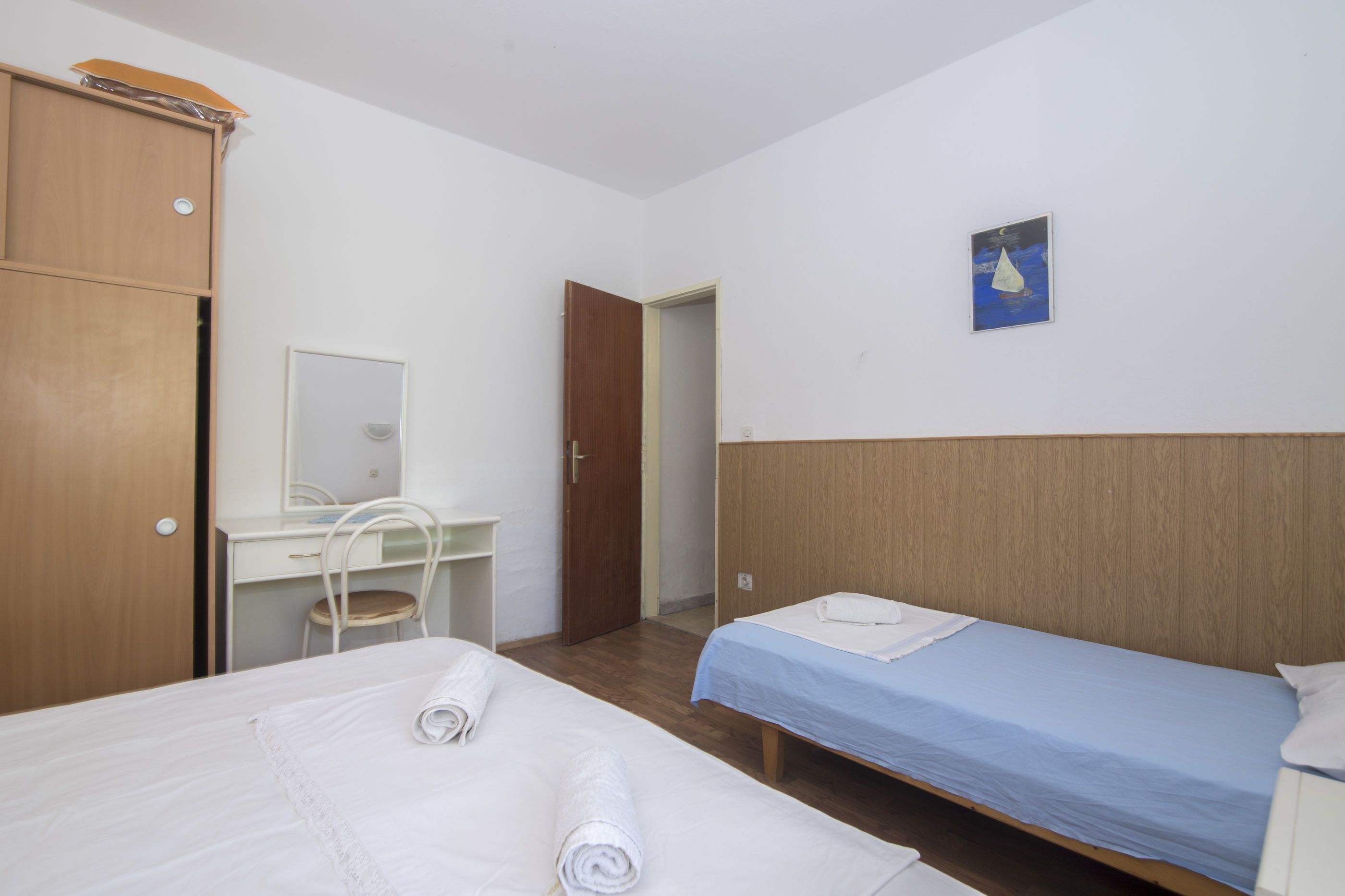 A bedroom with two beds, a desk, a chair, and a wardrobe.
