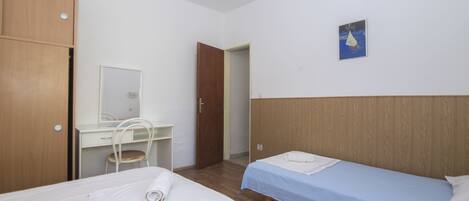 A bedroom with two beds, a desk, a chair, and a wardrobe.