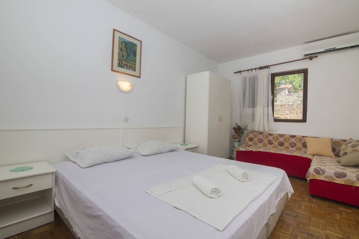A bedroom with a bed, a nightstand, a wardrobe, a sofa, and a window with curtains.