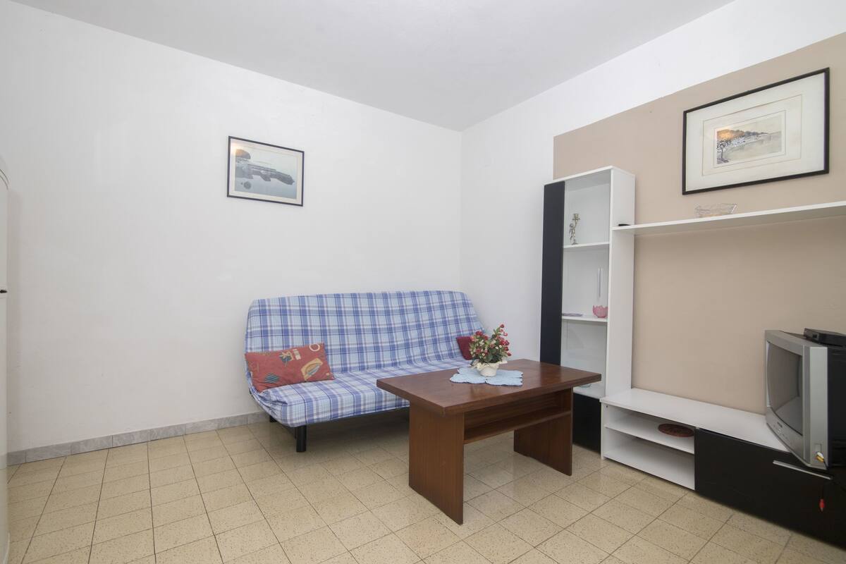 A small, furnished room with a blue plaid sofa, a wooden table, a television, and a bookshelf.