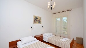 Ein Hotelzimmer mit zwei Betten, einem Holzkopfteil, einem Nachttisch, einem Gemälde und einem Fenster mit transparenten Vorhängen.