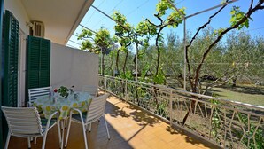 Ein Balkon mit Tisch und Stühlen, einem weißen Geländer und Blick auf Bäume und einen Garten.