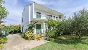Ein zweistöckiges Gebäude mit Balkon, Auffahrt und umliegender Bepflanzung.