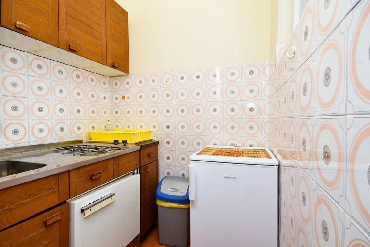 A compact kitchen with wooden cabinets, a gas stove, a white refrigerator, and patterned tiles.